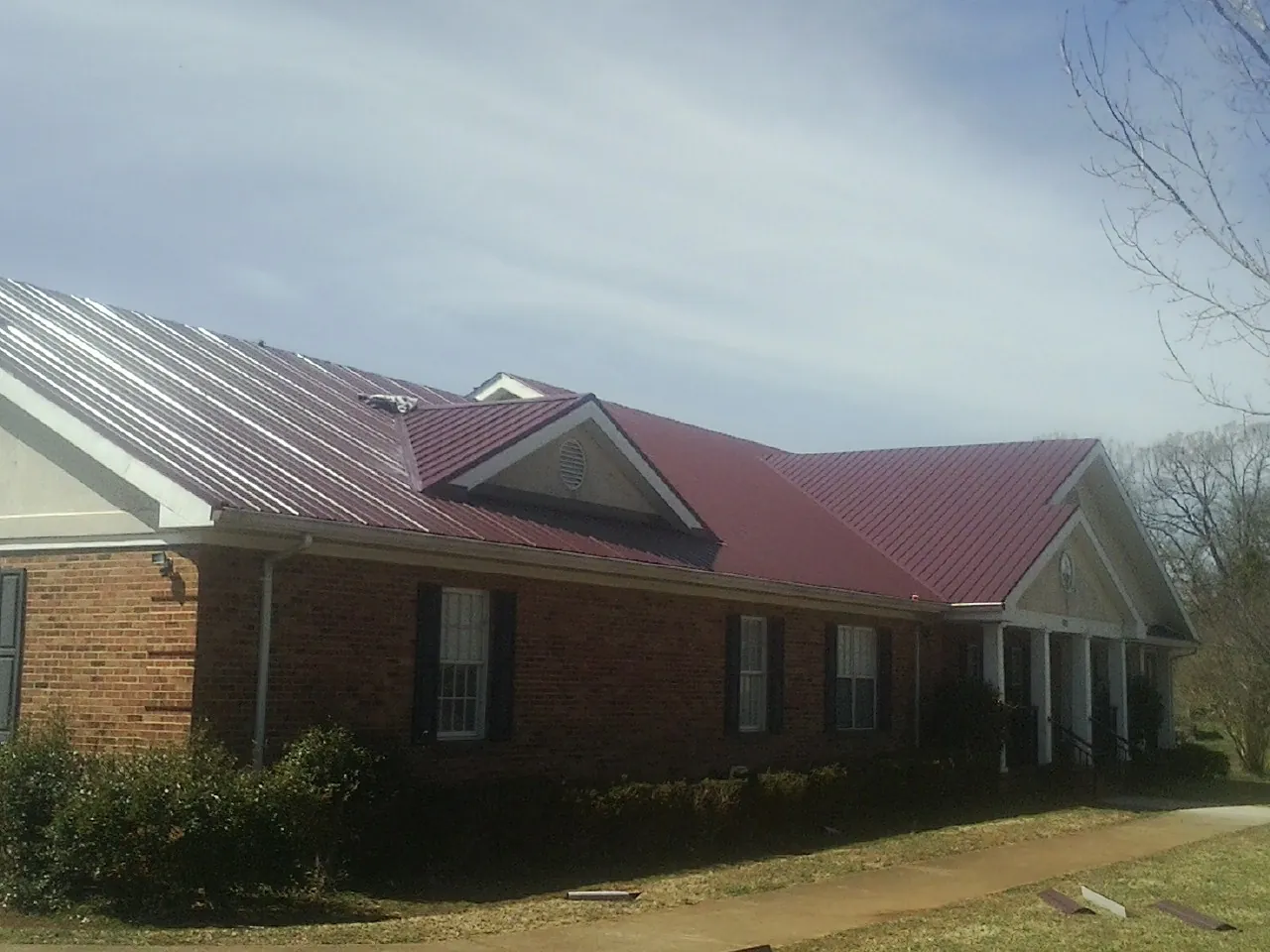 Red metal roof with gabled entries on a long brick building, from a Hail Damage Roof Repair job in Lexington