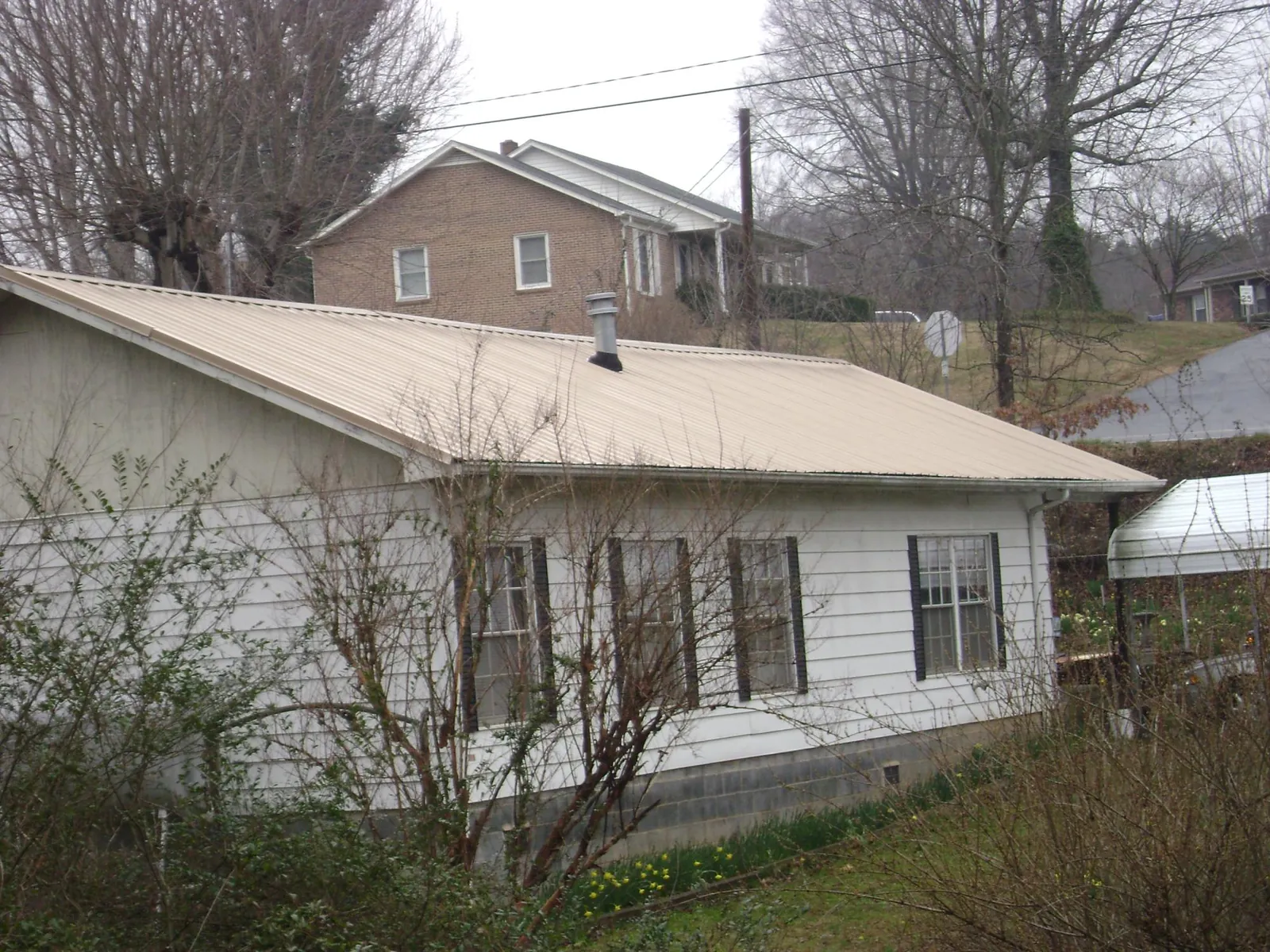 Tan metal roof on a white sided house set into a hillside — Commercial Roofing by Roofing Brothers in Lexington